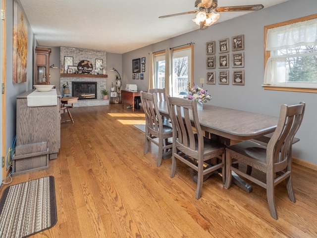 dining room featuring a fireplace, light wood-style floors, and ceiling fan