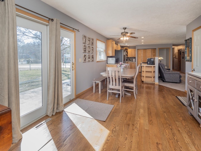 dining space with light wood-type flooring, baseboards, visible vents, and a ceiling fan