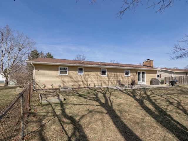 back of property with fence, a patio, a chimney, a yard, and a vegetable garden