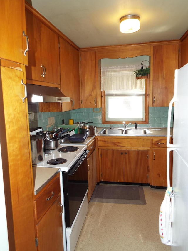 kitchen with a sink, under cabinet range hood, electric range oven, freestanding refrigerator, and light floors