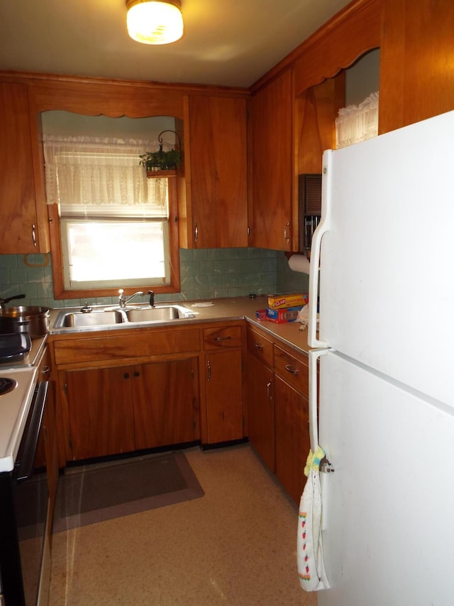 kitchen with brown cabinets, electric stove, a sink, backsplash, and freestanding refrigerator