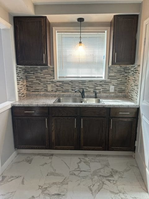 18635 Dale St, Detroit, MI 48219 - kitchen featuring dark brown cabinetry, marble finish floor, decorative backsplash, and a sink