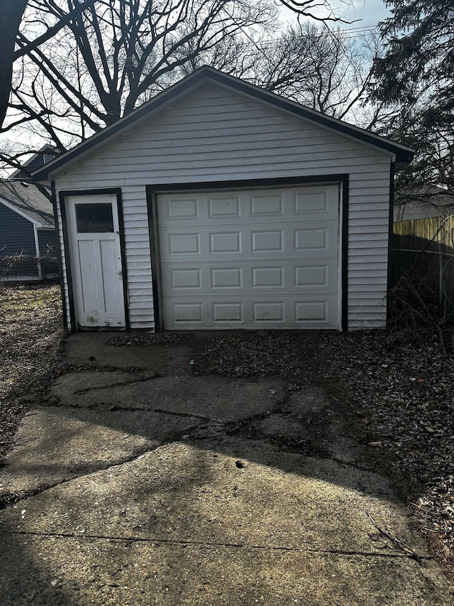 detached garage featuring concrete driveway and fence