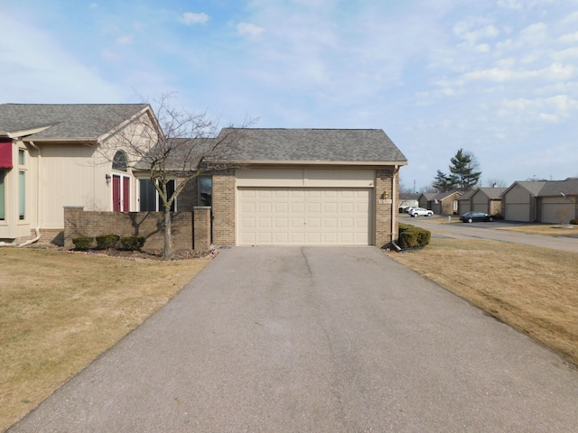 view of front of property with aphalt driveway, roof with shingles, a front yard, a garage, and brick siding