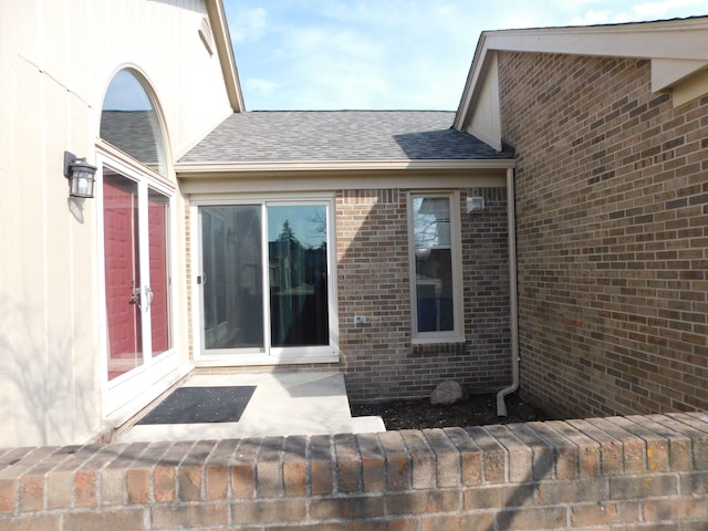 entrance to property featuring brick siding and roof with shingles