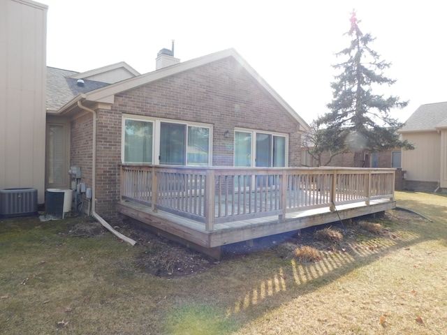 back of house with central air condition unit, brick siding, a chimney, and a lawn