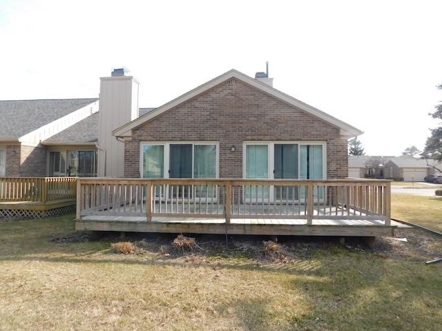 back of house featuring brick siding, a deck, a chimney, and a yard