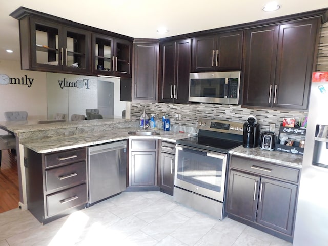 kitchen featuring a sink, tasteful backsplash, appliances with stainless steel finishes, a peninsula, and light stone countertops