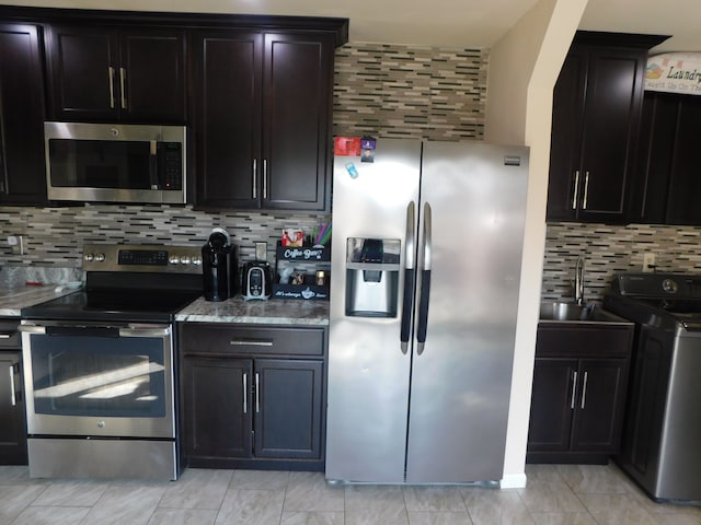 kitchen with stone counters, washer / clothes dryer, a sink, stainless steel appliances, and tasteful backsplash