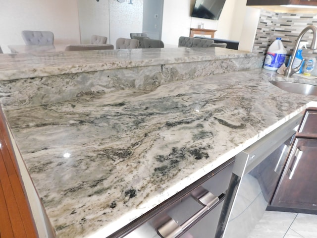 kitchen featuring a kitchen bar, a sink, light stone counters, tasteful backsplash, and stainless steel dishwasher