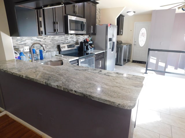 kitchen with a sink, light stone counters, decorative backsplash, stainless steel appliances, and separate washer and dryer