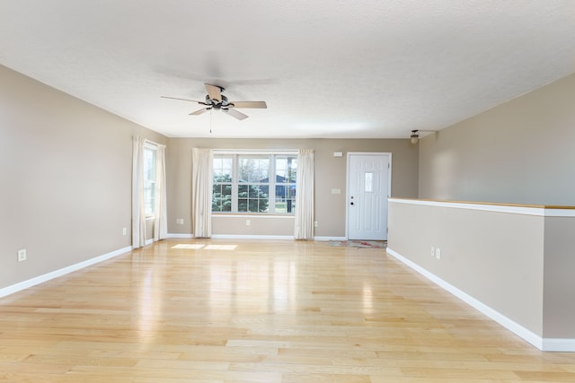 spare room with ceiling fan, baseboards, a textured ceiling, and light wood-style flooring