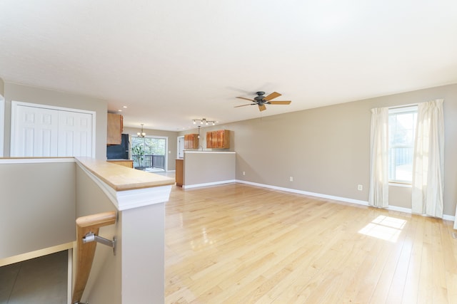 unfurnished living room featuring ceiling fan with notable chandelier, light wood-style floors, and baseboards