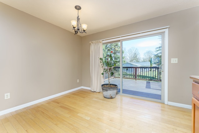 spare room with an inviting chandelier, baseboards, and light wood finished floors