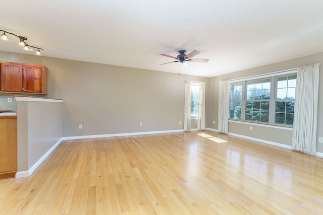 unfurnished living room featuring light wood finished floors, baseboards, and a ceiling fan