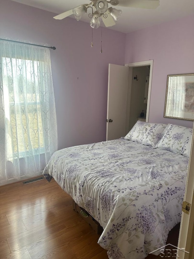 bedroom with wood finished floors, visible vents, and ceiling fan