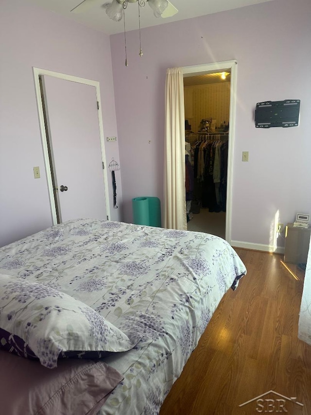 bedroom featuring a closet, baseboards, a walk in closet, and wood finished floors