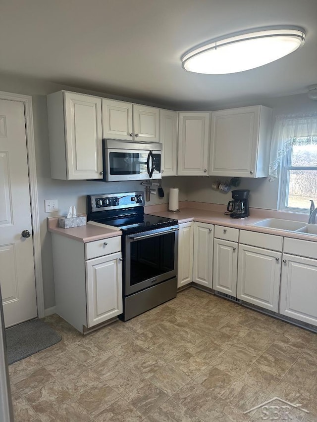 kitchen featuring white cabinetry, stainless steel appliances, light countertops, and a sink