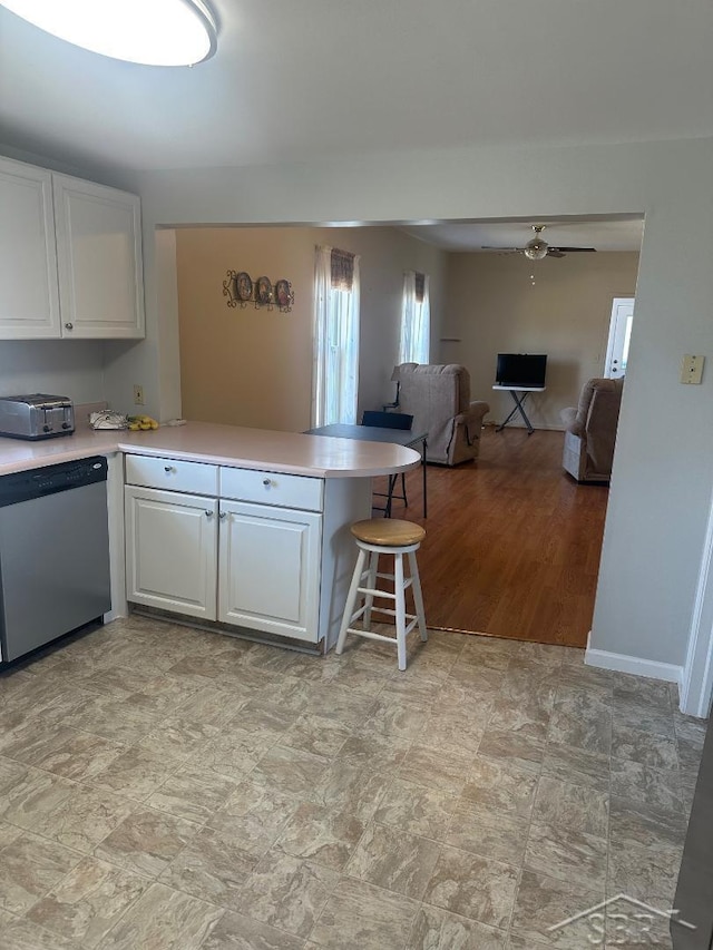 kitchen featuring stainless steel dishwasher, a peninsula, white cabinets, and light countertops