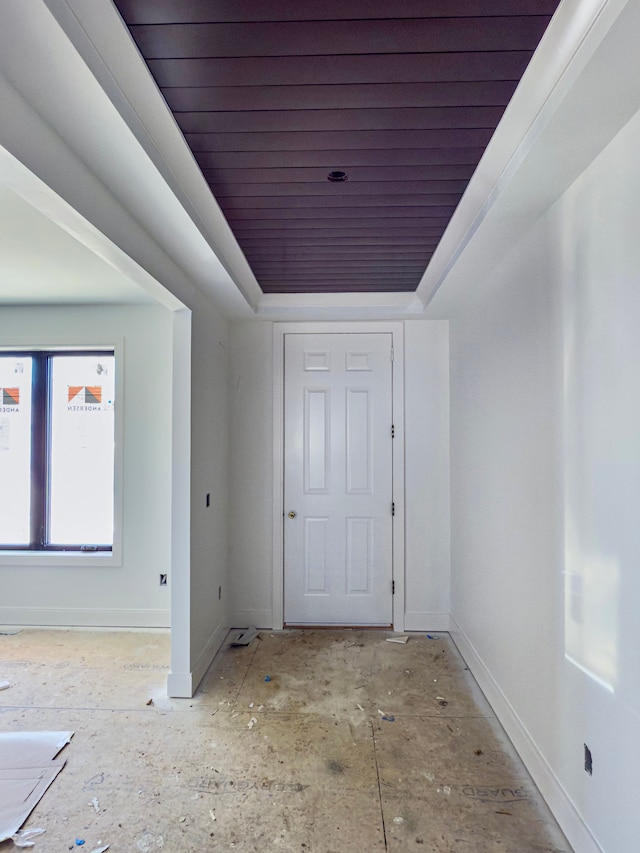 corridor featuring baseboards, a tray ceiling, and wooden ceiling