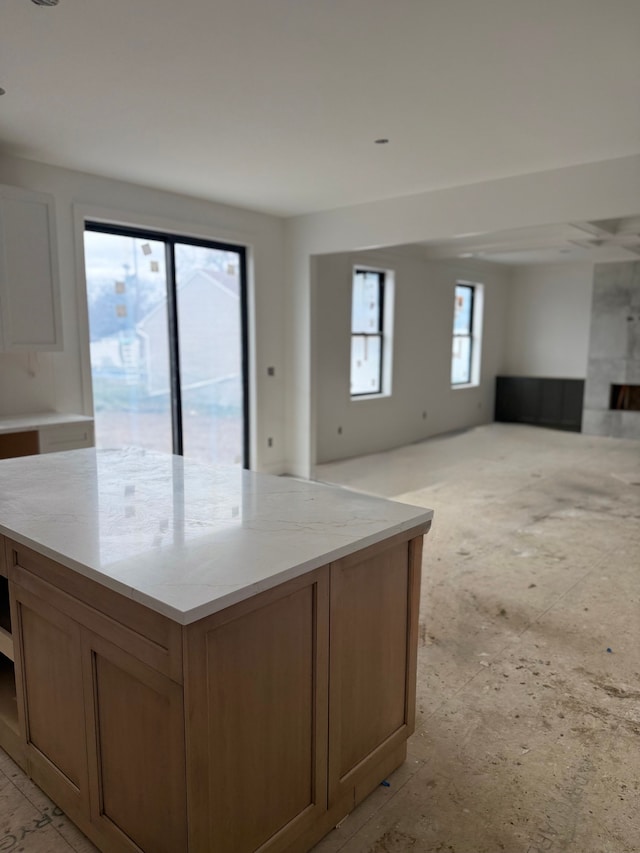 kitchen featuring open floor plan, a center island, light stone counters, and brown cabinetry