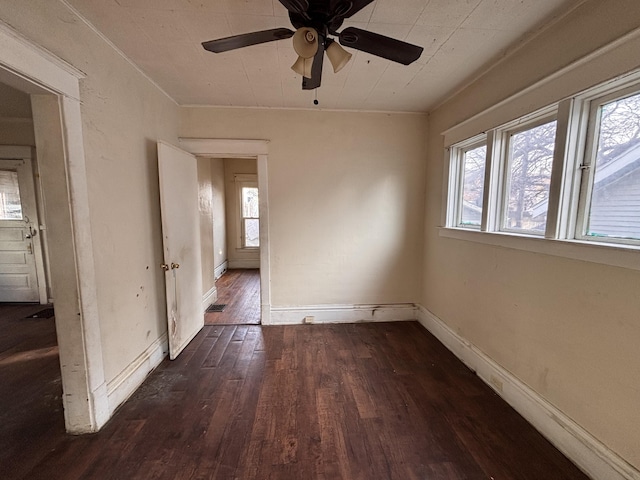 empty room featuring dark wood finished floors, baseboards, and a ceiling fan