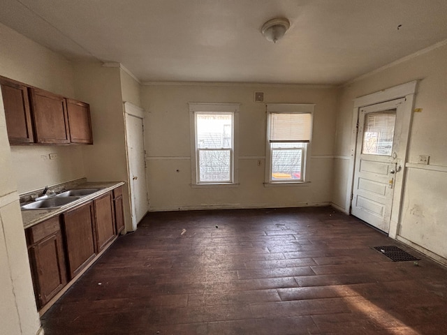 kitchen with visible vents, brown cabinets, dark wood-type flooring, a sink, and crown molding