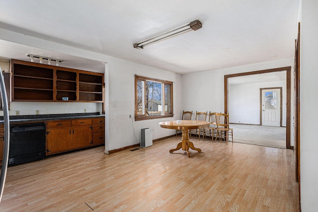 kitchen with brown cabinetry, open shelves, light wood-style flooring, black dishwasher, and dark countertops