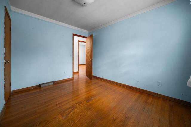 empty room with visible vents, baseboards, ornamental molding, and hardwood / wood-style flooring