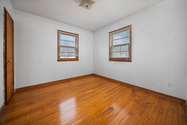 spare room featuring crown molding, plenty of natural light, light wood-style floors, and baseboards