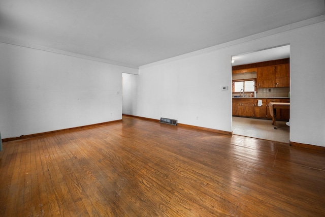 unfurnished living room featuring visible vents, a sink, wood-type flooring, crown molding, and baseboards