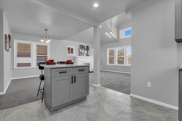 kitchen with gray cabinetry, a breakfast bar area, light carpet, a fireplace, and an inviting chandelier