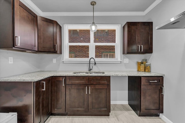 kitchen with dark brown cabinetry, ornamental molding, light stone counters, wall chimney exhaust hood, and a sink