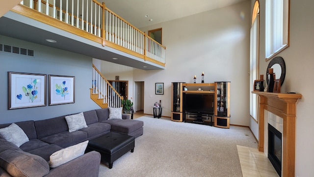 carpeted living room featuring visible vents, baseboards, a tiled fireplace, stairs, and a high ceiling