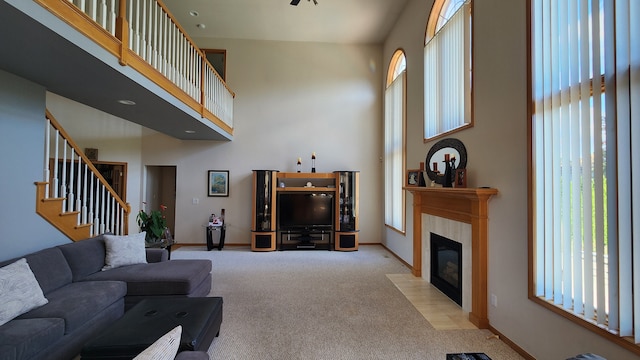 living room with light carpet, a healthy amount of sunlight, a tiled fireplace, and a high ceiling