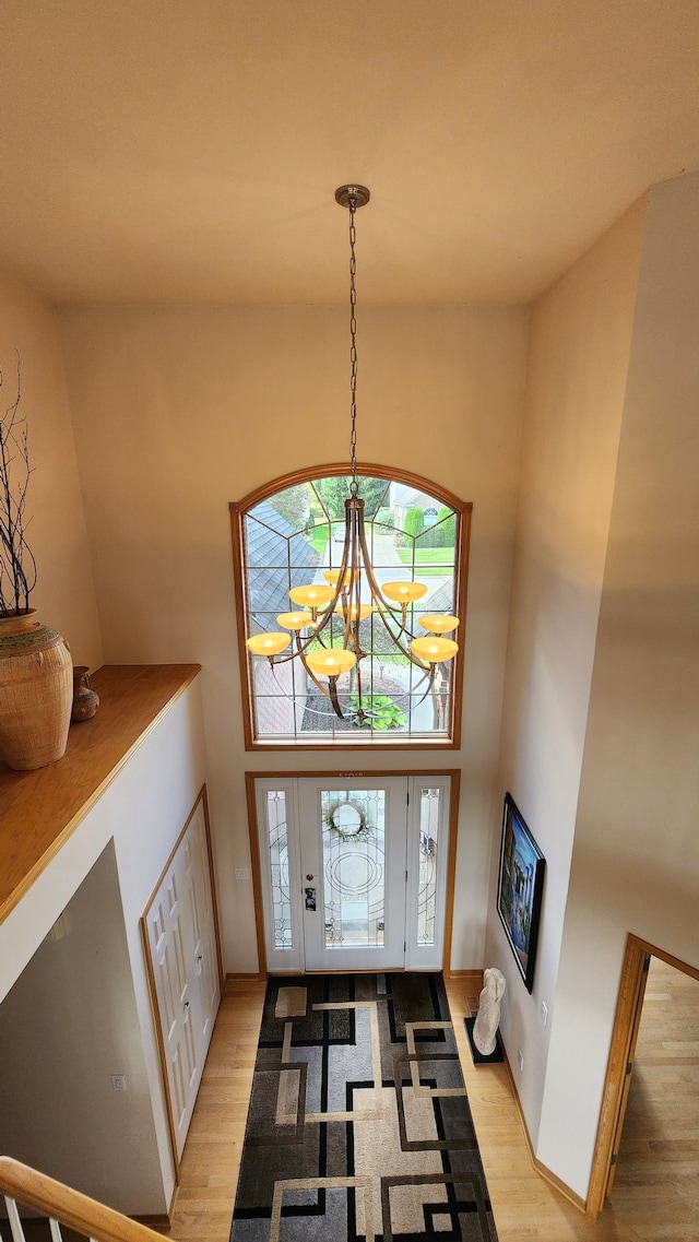 foyer with light wood-style flooring, a notable chandelier, and a towering ceiling