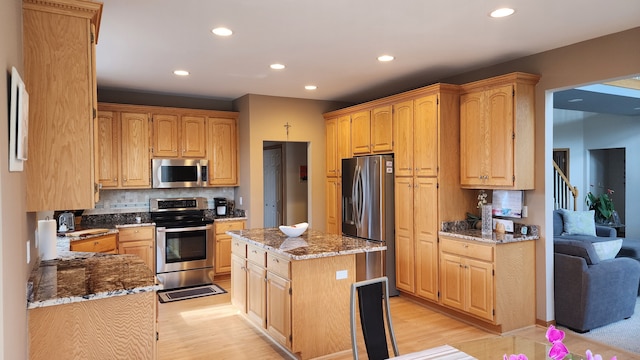 kitchen featuring stone countertops, decorative backsplash, appliances with stainless steel finishes, light wood-type flooring, and a center island