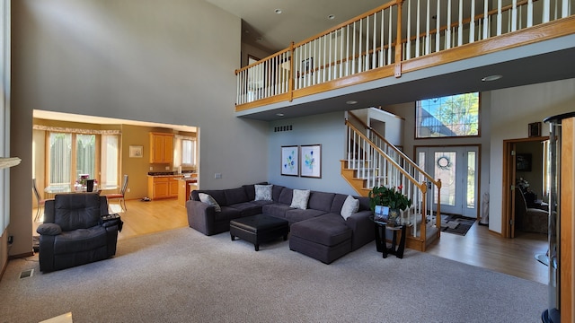 living area featuring stairway, light carpet, a high ceiling, and visible vents