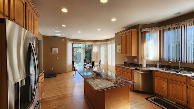 kitchen featuring light wood-type flooring, a sink, stainless steel appliances, brown cabinets, and a center island