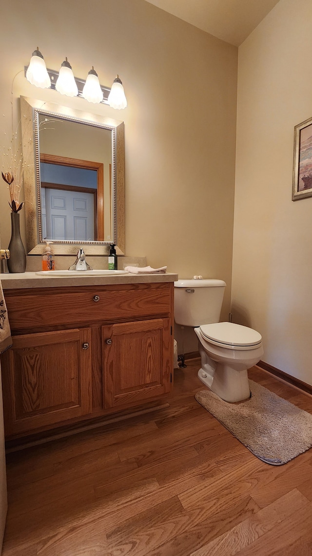 bathroom featuring baseboards, toilet, wood finished floors, and vanity