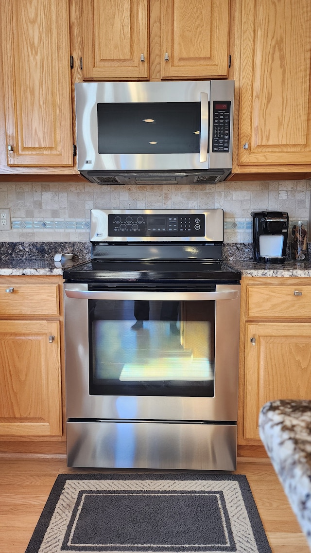 kitchen with dark stone countertops, backsplash, appliances with stainless steel finishes, and light brown cabinetry