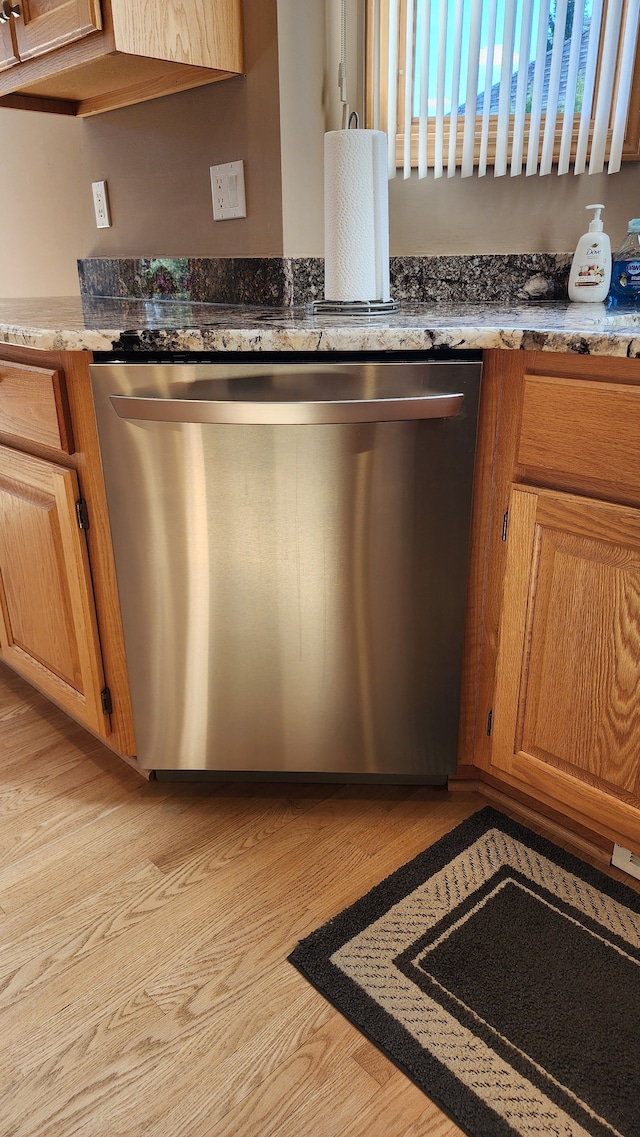 kitchen featuring stainless steel dishwasher, brown cabinetry, and light wood-type flooring