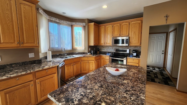 kitchen with brown cabinetry, dark stone counters, a sink, stainless steel appliances, and a center island