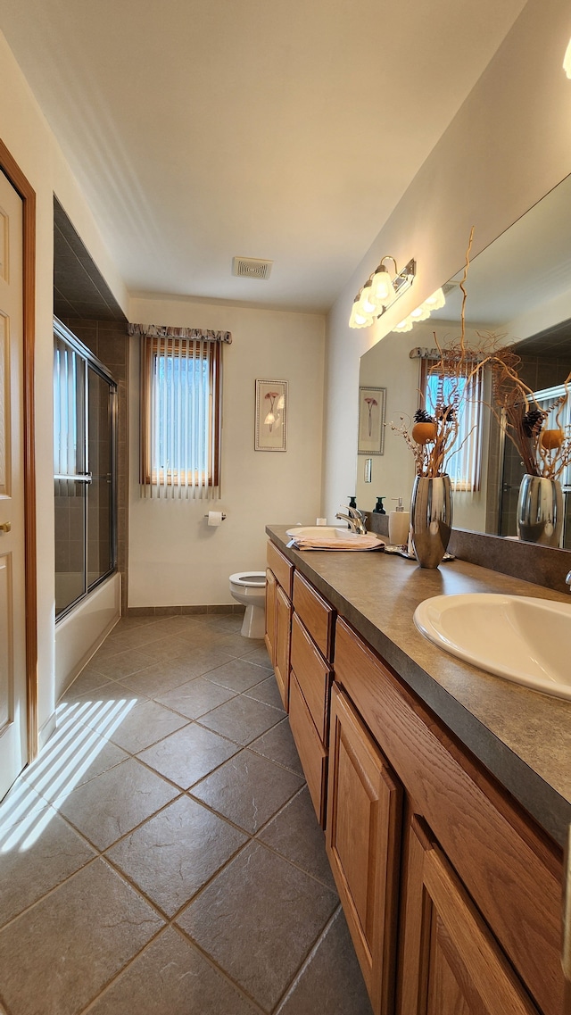 full bathroom featuring double vanity, toilet, combined bath / shower with glass door, and a sink