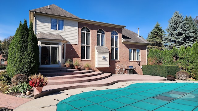 back of property featuring entry steps, a covered pool, roof with shingles, brick siding, and a patio area