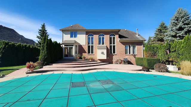 rear view of property with a covered pool, a patio, brick siding, and entry steps