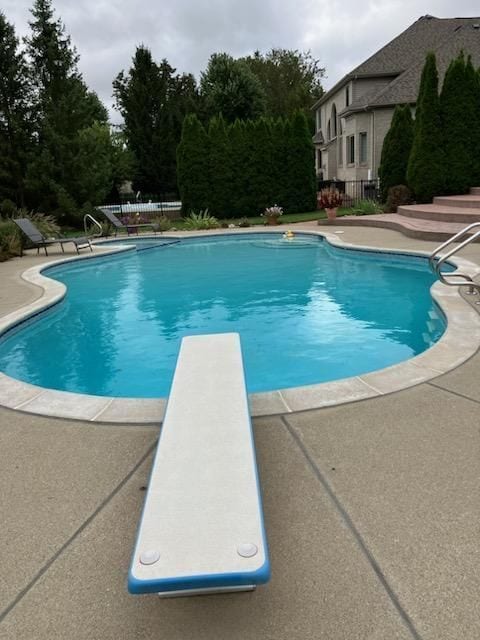 pool featuring a patio, fence, and a diving board