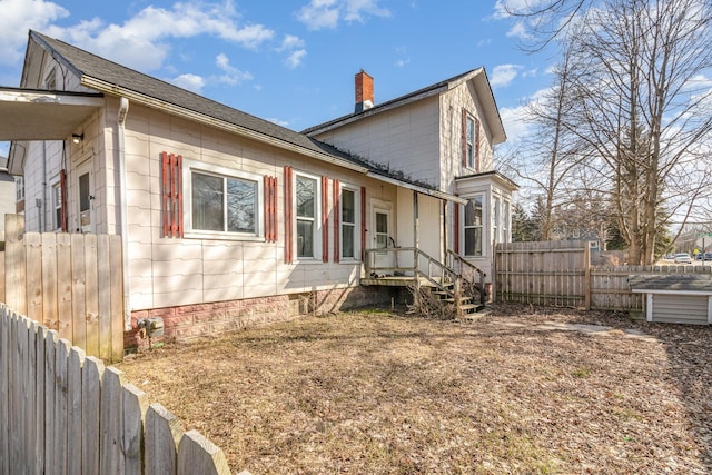 view of side of home featuring roof with shingles, a chimney, and fence