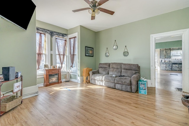 living area with baseboards, wood finished floors, and ceiling fan