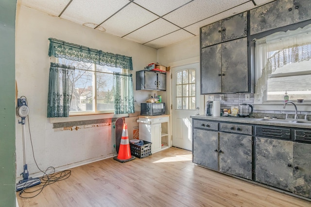 kitchen featuring a sink, a paneled ceiling, black microwave, and light wood finished floors